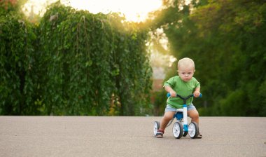 Cute little baby boy rides a balance bike in a summer park. Child learning to ride a bicycle
