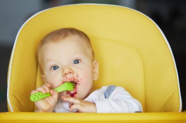 Bebeğin ilk beslenmesi. Çocuk sandalyeye oturur ve sebze püresi yer. Çocuk cerrahisinde ebeveynlik ve sağlıklı yemek kavramı