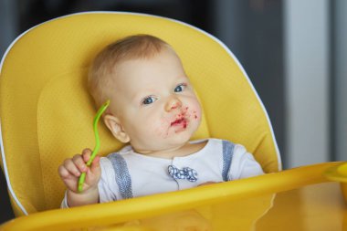 Bebeğin ilk beslenmesi. Çocuk sandalyeye oturur ve sebze püresi yer. Çocuk cerrahisinde ebeveynlik ve sağlıklı yemek kavramı