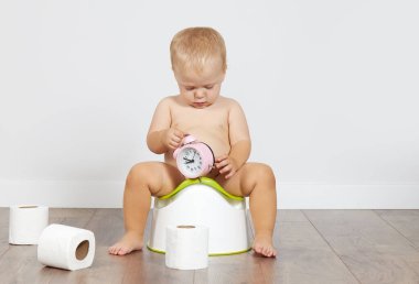 Cute baby boy sits on the potty with toilet paper in his hands. Potty training time
