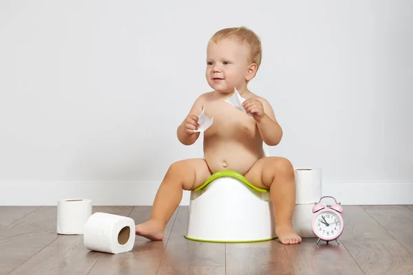 Cute baby boy sits on the potty with toilet paper in his hands. Potty training time