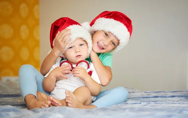 戴着圣诞老人帽子的可爱的孩子们在家里的床上玩耍很开心 哥哥和姐姐在等圣诞节假期 — 图库照片