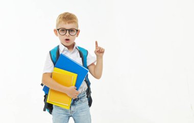 Okula dönelim. İlkokuldan beyaz bir arka planda kitap, sırt çantası ve gözlüğü olan komik bir çocuk. Neşeli bir şekilde gül. Okul için hazırlık. Erken gelişim kavramı