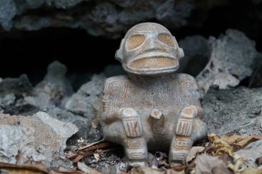 Taino Antika Taş Cemi Idol figürü yakınlarda yaprakları olan bir mağarada oturuyor. Taino Hint Mitolojisi.