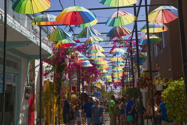 Dominik Cumhuriyeti, Puerto Plata, Şemsiye Caddesi, 29.06.2022, Güneşli yaz gününde renkli şemsiyeler altında gürültülü bir turistik sokakta insanlar