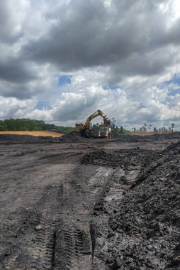 Güneşli ve bulutlu bir günde kazıcı kamyona yüklenirken açık kömür madenciliği etkinliği. Berau, Endonezya. 22 Haziran 2022