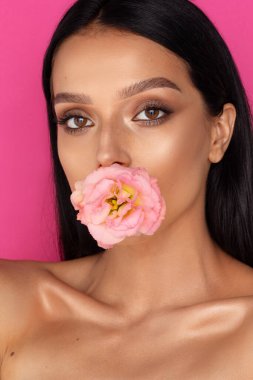 Güzel esmer kadın portresi, ağzında pembe bir çiçek, pembe arka plan.