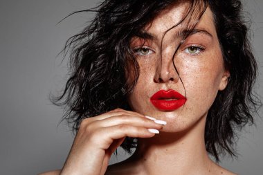beauty young woman face with a lot of freckles and red lips, hand near face, close up