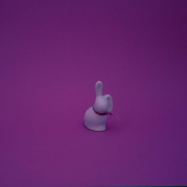 Mor arka planda dekoratif kurdeleli bir tavşanın seramik figürü. Düz konsept.