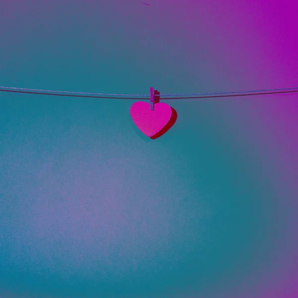 Little heart attached with clothespins on wire on a blue pink background.