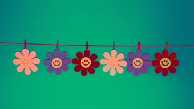 Yeşil arka planda çengelli mandallarla bağlanmış renkli çiçekler.