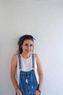 Kendine güvenen, gülümseyen ve ifade veren, kameraya gülümseyen, beyaz tulumlu, beyaz gömlekli, beyaz arka planlı güçlü bir kadın. uygun vücut ile