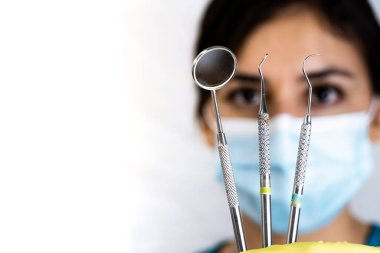 young female dentist holding dental instruments in her hand, protected by a glove on a white background and wearing a mouth cover.
