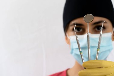 young female dentist holding dental instruments in her hand, protected by a glove on a white background and wearing a mouth cover.