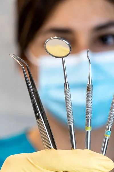 young female dentist holding dental instruments in her hand, protected by a glove on a white background and wearing a mouth cover.