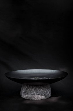 bowl with metal water and natural stone base, works as a water mirror, decoration, design. Black background with natural filtered light, the stone is terrazzo, quarry or recinto. Works as a pot or