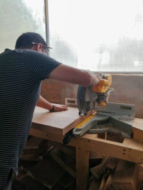 A man cuts wood on a circular saw in a joinery, A man cuts wood on a circular saw in a joinery, band saw, holding a plank, two-inch wood plank being cut, in a woodworking shop