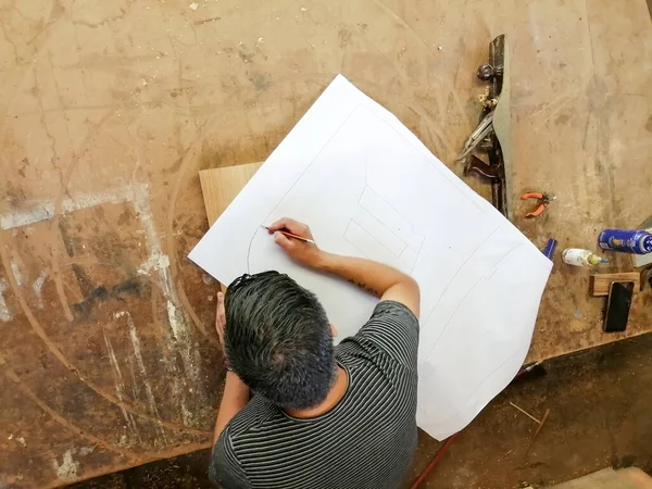 一位无名氏木匠在他的工作室里为新项目工作 坐在工作台前 用铅笔和尺子在纸上画新零件的难以辨认的人的桌面视图 — 图库照片