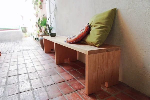 wooden bench, with cactus, cushions and plants. Natural clay floor, white painted wall