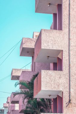 pink building with balconies, palm tree between modules, light cables in the space. Rough wall finish