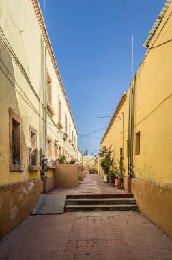 central courtyard of a neighborhood, yellow houses with brick, stairs and ramp, potted plants outside, clear blue sky. mexican neighborhood, mexico
