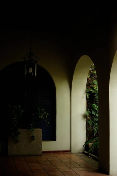 colonial architecture, arches surrounded by vegetation, play of light and shadows inside the space, natural materials, clay floor, ceiling lamp and red brick.