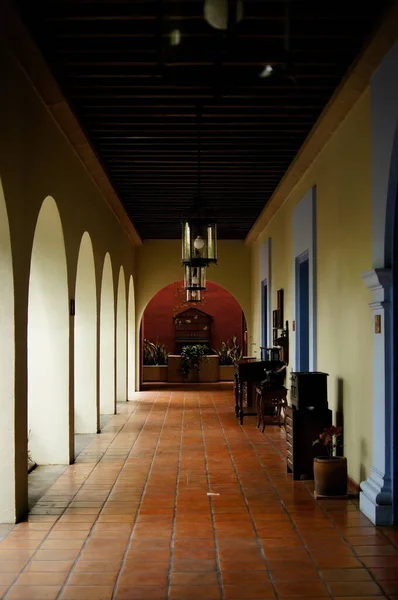 colonial architecture, arches surrounded by vegetation, play of light and shadows inside the space, natural materials, clay floor, ceiling lamp and red brick.