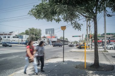 two people crossing the street with a yellow cross, in the background the city, gas stations, cars, cables and buildings.