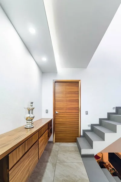 distributor of a modern house, with stairs and light at the foot, wooden storage cabinet, door to a natural wood room. White paint, guadalajara, mexico