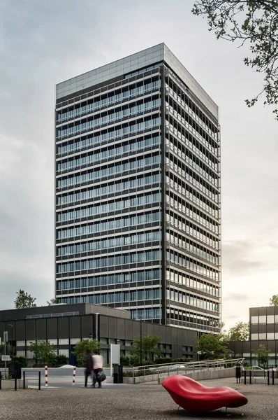 Modern tall glass building in the posh embassy tech village area, workers carrying dustbin walking towards building on pathway, with cars and ten in blurred motion