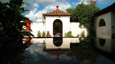 colonial architecture, arches surrounded by vegetation, play of light and shadows inside the space, natural materials, clay floor, ceiling lamp and red brick.