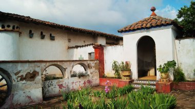 colonial architecture, arches surrounded by vegetation, play of light and shadows inside the space, natural materials, clay floor, ceiling lamp and red brick.