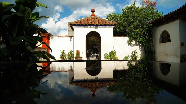 colonial architecture, arches surrounded by vegetation, play of light and shadows inside the space, natural materials, clay floor, ceiling lamp and red brick.