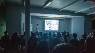 students paying attention to a lecture given by a woman, projecting about books and architectural education, students taking notes and taking pictures.