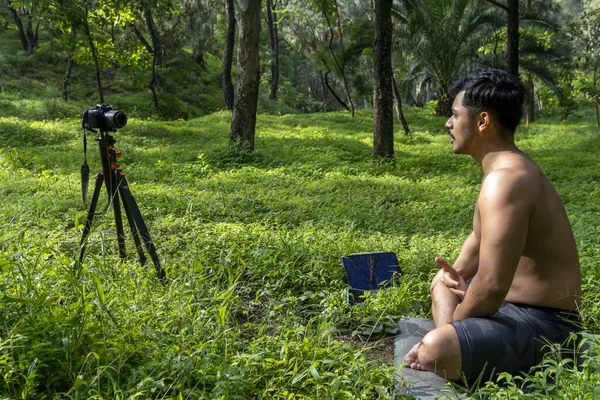View of a man conducting virtual fitness class with group of people at home on a video conference. Fitness instructor taking online yoga classes over a video call in laptop. use of tripod and camera to broadcast the yoga class