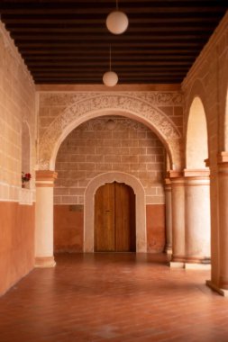 colonial architecture, arches surrounded by vegetation, play of light and shadows inside the space, natural materials, clay floor, ceiling lamp and red brick.