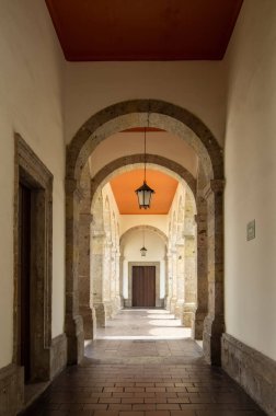 colonial architecture, arches surrounded by vegetation, play of light and shadows inside the space, natural materials, clay floor, ceiling lamp and red brick.