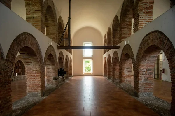 colonial architecture, arches surrounded by vegetation, play of light and shadows inside the space, natural materials, clay floor, ceiling lamp and red brick.