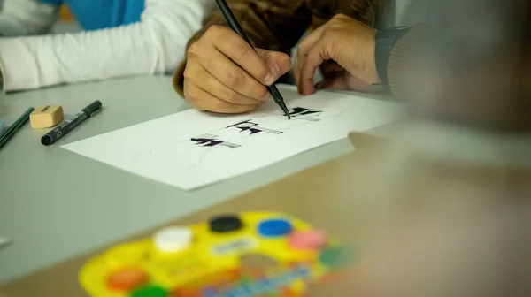 person drawing by hand with pen, pencil and ink, architectural perspectives, in color. Drawing on paper on a drawing board or desk.