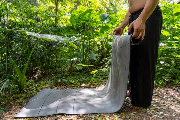 young brown latin man, rolling up his mat to exercise in the forest, surrounded by vegetation, latin america