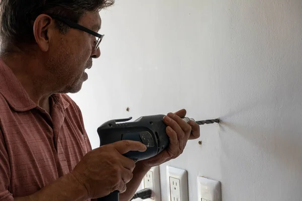 latin man in his 50s, drilling a wall with a drill, white wall, mexico latin america