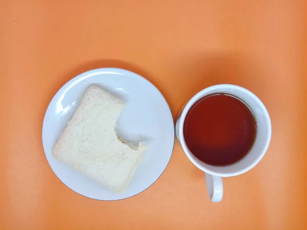 Uma Xícara Chá Pedaço Mordido Pão Branco Isolado Fundo Laranja — Fotografia de Stock