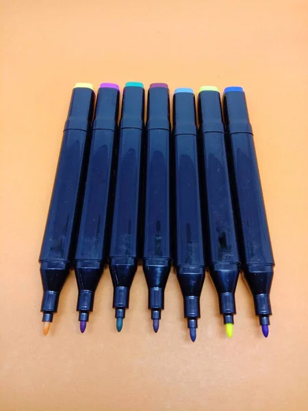 row of coloring pens to color the paintings in the drawing book,isolated on an orange background.