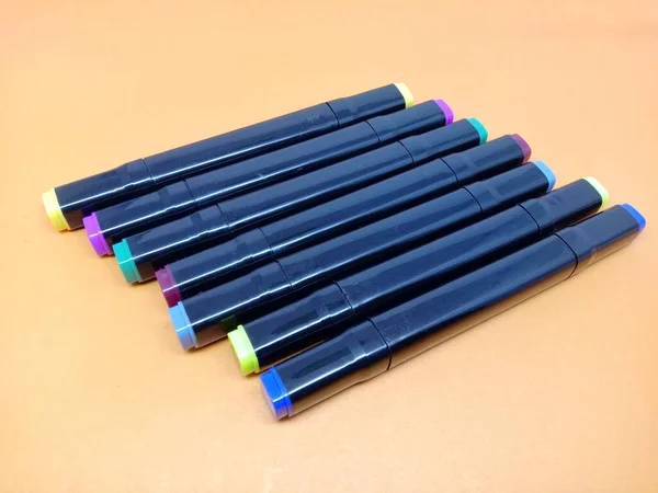row of coloring pens to color the paintings in the drawing book,isolated on an orange background.
