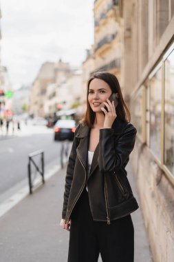 Şık ceketli neşeli genç kadın Paris 'te sokakta akıllı telefondan konuşuyor. 