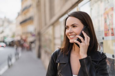 Şık ceketli neşeli genç bir kadının portresi Paris 'te sokakta akıllı telefondan konuşuyor. 
