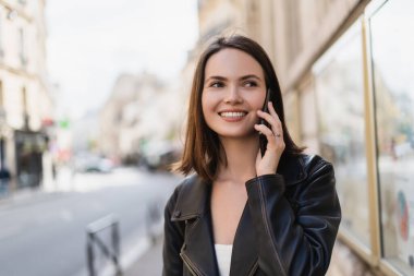 Şık ceketli gülümseyen genç bir kadın Paris 'te sokakta akıllı telefondan konuşuyor. 