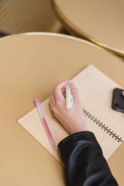 Yuvarlak masa üzerinde boş defterin yanında kalem tutan kadının kırpılmış görünümü 