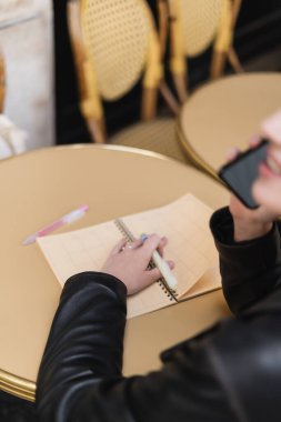 Akıllı telefondan konuşan, yuvarlak masada bulanık bir defter gören bir kadın.