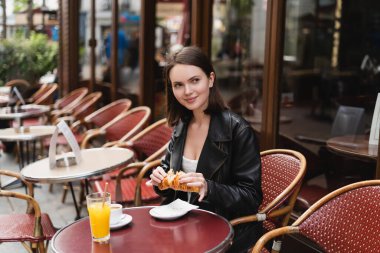Neşeli bir kadın, Paris 'te açık bir kafede bir fincan kahve ve bir bardak portakal suyu yanında kruvasan tutuyor.